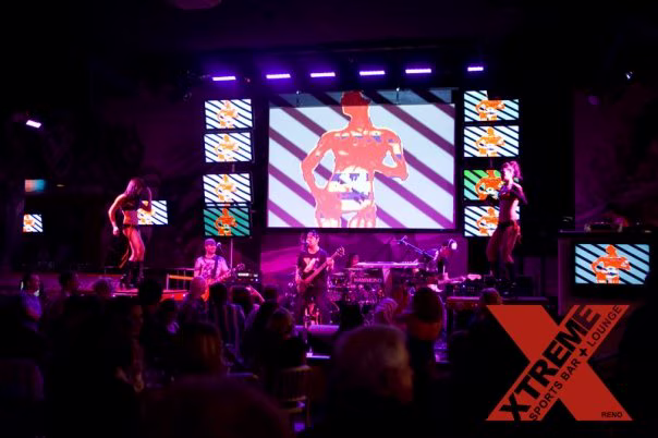 XTREME nightclub stage with a live band, go-go dancers, a large projection screen and four stacked television screens on each side